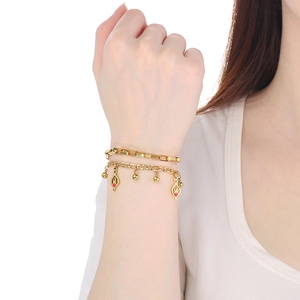 Close-up of gold double-layer bracelet with red heart and ball charms on model wrist