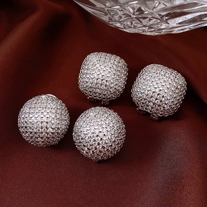 Macro detail of silver pave-set zircon ball earrings on a dark red satin background