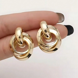 Exaggerated geometric gold interlocking hoop earrings held between fingers for size comparison