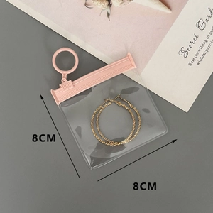 Macro shot of 8x8cm transparent EVA jewelry pouch with pink seal holding gold hoop earrings