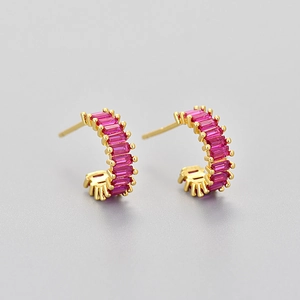 Close-up of golden C-shaped hoop earrings with sparkling pink rectangular zircons