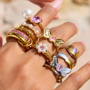 Close-up of stacked rings featuring pink zircon, pearls, and golden butterfly details
