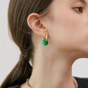 Close-up of a gold hoop earring with green agate pendant on a model's ear