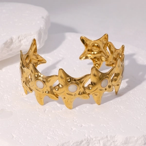 Gold starfish open cuff bracelet with white stone inlays on a white stone background