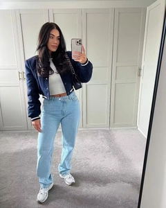 Full view of a dark blue cropped baseball jacket paired with light blue jeans and sneakers