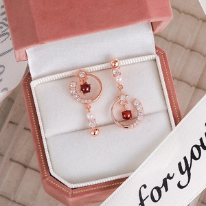 Detailed view of asymmetric star and moon earrings with pink stones and pearls in a box
