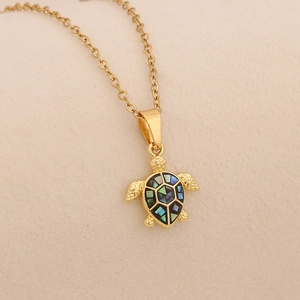 Golden stainless steel necklace with natural shell sea turtle pendant on beige fabric
