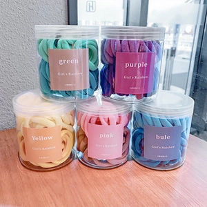 Five jars of colorful high-elastic hair ties for girls in rainbow colors on a wooden table