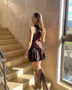 Schickes braunes ärmelloses Kleid mit Rüschensaum und braunen Stiefeln auf einer Treppe