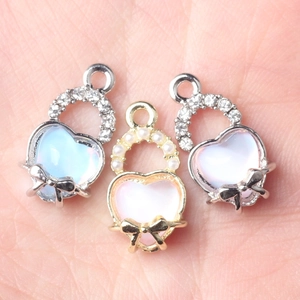 Delicate heart-shaped charms with rhinestones and pearls held in palm for DIY jewelry
