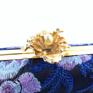 Detail of golden metal flower clasp with pearl on navy blue embroidered evening clutch