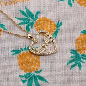 Collier avec pendentif cœur LOVE en cuivre doré et zircone sur fond à motif ananas