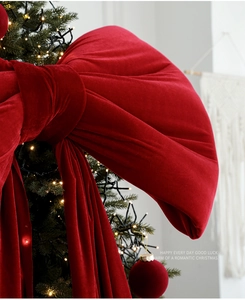 Detail of a large red velvet bow hanging on a lit Christmas tree for festive decor