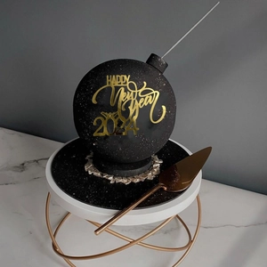 Detail of black bomb-shaped cake with golden Happy New Year 2024 acrylic topper