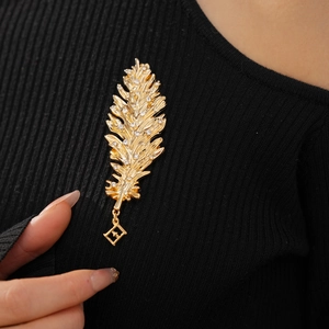 Detail of leaf feather brooch with crystals and geometric pendant on black sweater