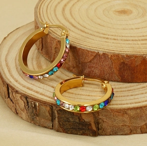 Macro detail of 18K gold-plated hoop earrings with multi-colored crystals on wood base