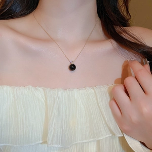 Close-up of a gold necklace featuring a polished black pearl and a small zircon stone