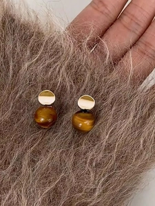 Detail of 18k gold plated stud earrings with brown tiger eye stone on faux fur background