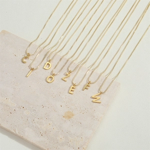 Macro detail of 14K gold plated capital letter pendants on fine minimalist box chains