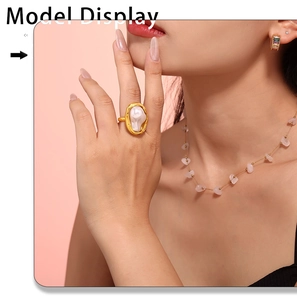 Irregular pearl ring with wide gold band shown on a model's hand in soft pink lighting