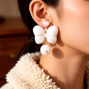 Detail of elegant white fabric bow earring with heart pearl stud and soft pom-pom drop