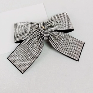 Detail of a black bow hair clip with sparkling white rhinestones on a clean grey surface