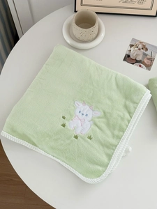 Close-up of light green plush towel with delicate white lamb embroidery and braided edges