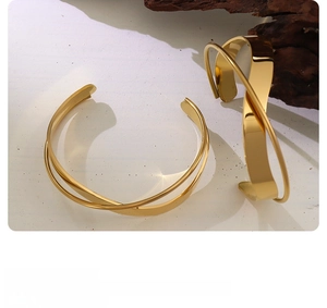 Detailed view of crossover 18K gold plated bangle on a white marble stone surface