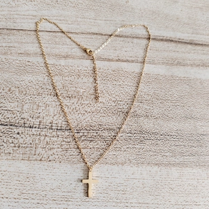 Close-up of a minimalist 18K gold stainless steel cross pendant on wood background