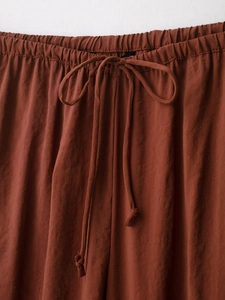 Close-up of the elastic waistband and drawstring detail on rust-red draped trousers