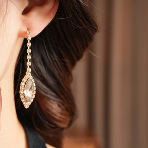 Detailed close-up of a long golden tassel earring with sparkling teardrop crystal and rhinestones