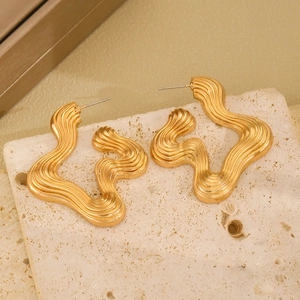 Detailed view of large golden wave shaped earrings with a smooth polished metallic finish