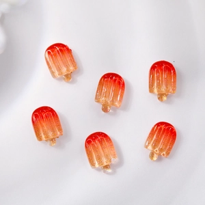 Macro view of six orange gradient resin popsicle nail art charms on white fabric background