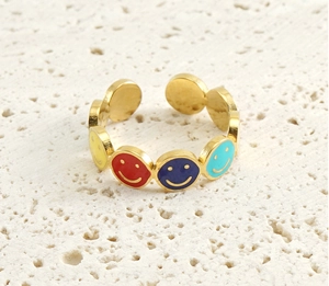 Macro detail of gold-plated open ring with multi-colored enamel smiley faces on stone texture