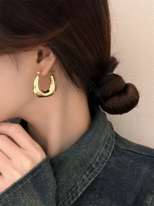 Boucles d'oreilles créoles en U dorées sur mannequin au design géométrique minimaliste