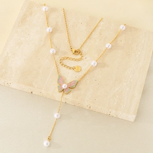 Detailed macro of gold Y-shaped butterfly necklace with pink enamel and white pearls