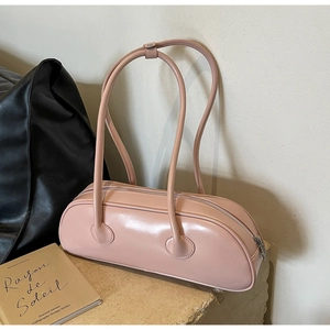 Detailed side view of a pink cylindrical shoulder bag with thin straps on stone