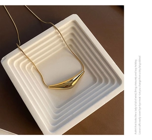 Détail d'un collier chaîne serpent dorée avec un pendentif géométrique au poli miroir