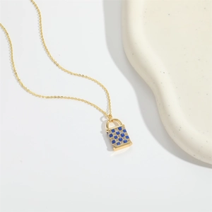 Detailed close-up of a blue checkered enamel gold lock pendant necklace on a ceramic tray