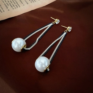 Detail view of long tassel earrings with white pearls and gold chains on velvet background