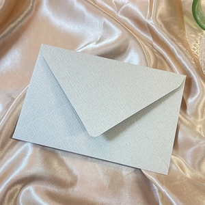 Detail showing the textured light blue linen paper envelope on elegant champagne silk fabric