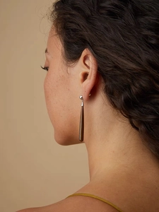 Close-up of a long brown wood grain teardrop earring worn by a model in soft lighting