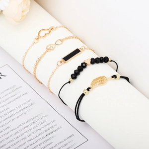 Detail of five-piece gold and black bracelet set with heart, infinity, and leaf charms