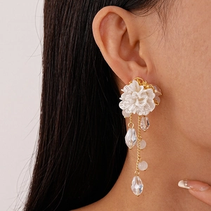 Elegant white acrylic flower earrings with golden tassels and crystal beads on a model