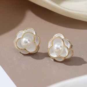 Macro detail of white enamel camellia stud earrings with gold edges and a center pearl