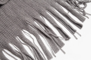 Close-up of grey knitted shawl with detailed striped texture and fringe tassels
