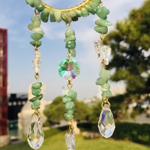 Macro view of green crystal stones and clear teardrop pendants on a gold moon sun catcher