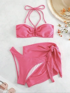 Detailed flat lay of pink ribbed three-piece bikini set with matching tie skirt on marble