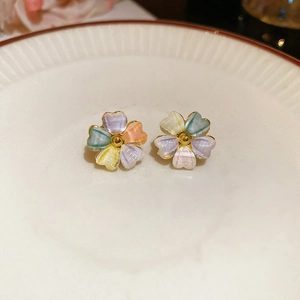 Close-up of colorful acrylic flower stud earrings with 18k gold beads on a white plate