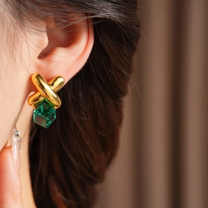 Close-up of vintage gold X-shape earrings with emerald green crystal cubes on model
